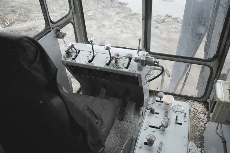 Liman "ohjaushytti". Noiden vipujen merkityksestä osaan sanoa sen verran (en ole koskaan tämän merkkistä konetta ajanut), että vasemman puoleinen kiiltäväksi kulunut vipu on ylävaunun kääntö. Keskimmäinen on vetovaijeri ja oikean puoleinen kiiltävä nuppi on nostovaijeri. Ohjauspöydän alla on veto- ja nostovaijereiden jarrujen polkimet. Tämä järjestys on tyyppillinen amerikkalaisissa koneissa ja on mielestäni mukavampi kuin esim. Lokomolaisissa oleva järjestys, jossa ylävaunun kääntö on veto- ja nostovipujen välissä. Lokomon järjestys johtaa siihen, että käsiä tulee hämmennettyä enemmän puolelta toiselle. Nosto- ja vetovaijereiden vipujen sivussa näkyy pultattuna eräänlaiset kulissit, joiden avulla vinssauksen voi jättää alalaidassa päälle "pykälään". Pöydässä äärimmäisenä oikealla oleva kiiltävä hanikka on luullakseni kaasuvipu. Korjatkaa te, jotka tiedätte paremmin. Sen vasemmalla puolella olkeva lyhyt himmentynyt vipu on ilmeisesti puomin nosto ja lasku ja sen vieressä puomin noston säppilukon ilmaventtiili. Oikenpuoleisessa pöydässä on sitten teloilla ajoon liittyviä ohjausvipuja.