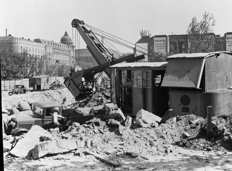 Vanhaa kasarmialuetta kunnostetaan linja-autoasemaksi Heikinkadun, nykyisen Mannerheimintien kohdalla ja samalla risteysalueelle tehdään myös uusia viemäröintejä, kaivinkoneen merkintä H.K.R. 5 tarkoittaa, että kone on Helsingin Kaupungin Rakennusviraston kaivinkone numero 5. kone on mahdollisesti moottorikäyttöinen, koska höyrykoneen kattilan savupiippua ei ainakaan kuvassa näy, toinen vaihtoehto on että koneessa on poikittainen höyrykattila, jonka savutorvi tulee ulos vasemman sivuseinän takapäästä ja ei siksi näy kuvassa, taaempana moottorikäyttöinen kraana, kuva: Foto Roos, vuosi: 1935, Helsingin kaupunginmuseo.