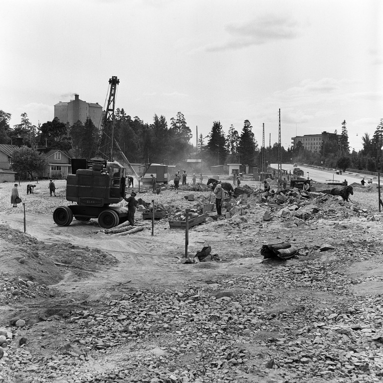 Sama työmaa, maassa näkyy jassikoita, joihin kivet ja maa lapioidaan miesvoimin, nosturin avulla jassikat nostettiin kuorma-auton lavalle ja jassikka kipattiin tyhjäksi irrottamalla avoimen pään koukut, tällä työmaalla näkyy myös kaksi hevosta kärryineen, joita kätettiin vielä tähän aikaan jopa maanajossa, kuva: Okkola Bertel, Helsingin kaupunginmuseo.