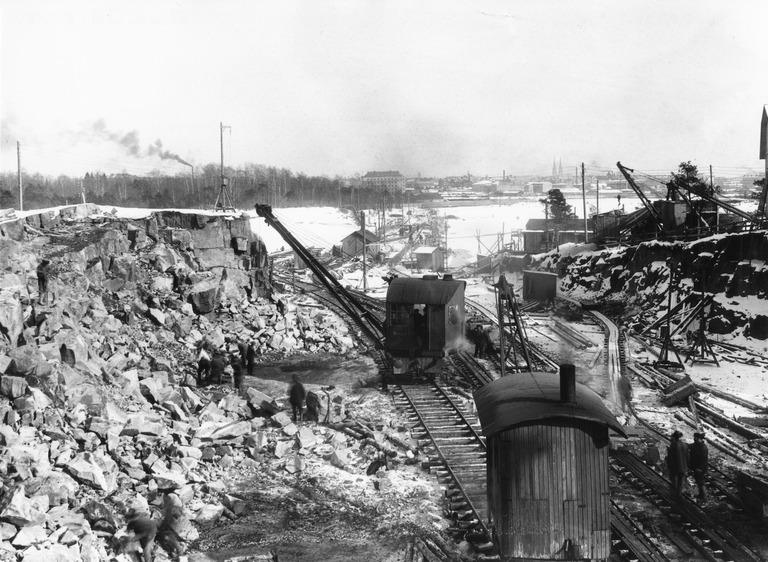 Sataman rakennustöitä Jätkäsaaressa 1910-1919 välillä, kaksi höyrykraanaa kalliolouhoksella, kallioiden louhimisesta oli hyötyä kahdella tavalla: epätasaisen mäen sijaan saatiin tasaista kenttää ja louhittuja kiviä voitiin käyttää laitureiden, rakennusten ja ratojen tekoon, kuva Rosenberg Harald, Helsingin kaupunginmuseo.