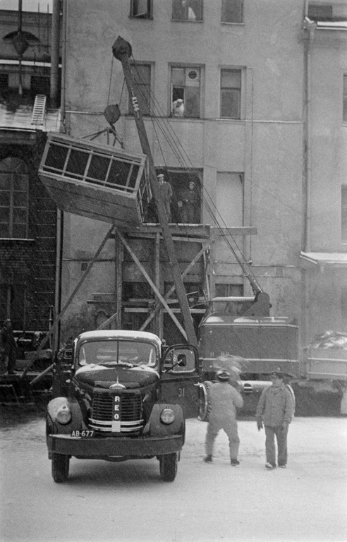 Uusia maitosäiliöitä nostetaan nosturilla ikkunan ja osittain puretun seinän kautta sisään Elannon meijeriin. Reon vieressä oleva mies näyttää viittilöivän vimmatusti (kuvassa pitkä valotusaika). Kuva Helsingin kaupunginmuseo.
