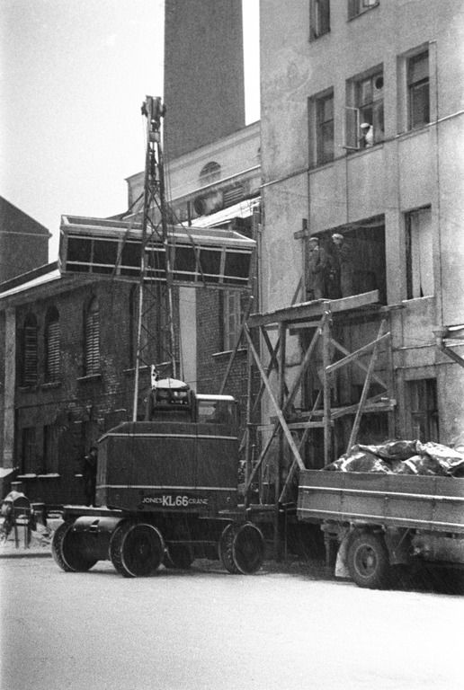 Uusia maitosäiliöitä nostetaan nosturilla ikkunan ja osittain puretun seinän kautta sisään Elannon meijeriin vuonna 1954 tai 1955. Nosturina on Jones KL 66. Kuva Helsingin kaupunginmuseo.
