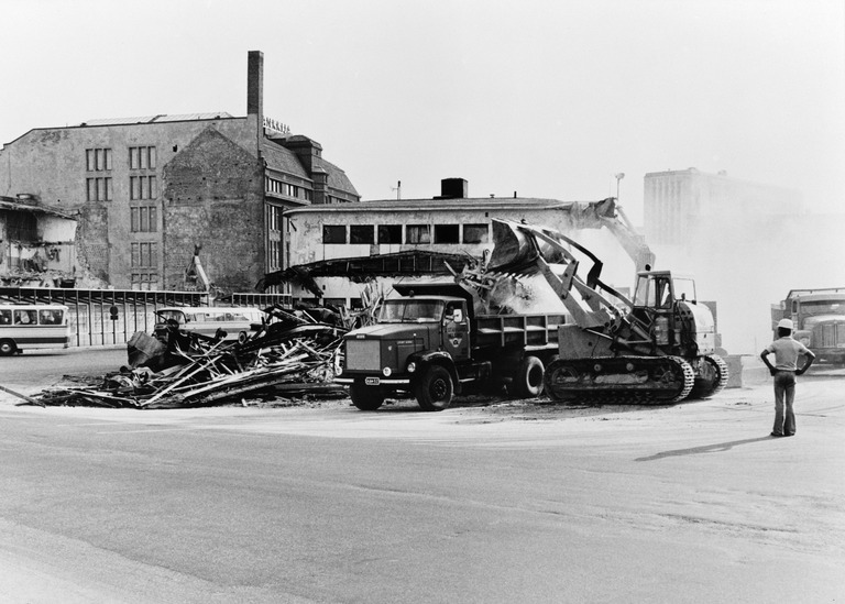 Shellin huoltoasemaan Kampin linja-autoaseman vieressä puretaan 1973. Caterpillar Traxcavator 977 lastaa. Viereisellä tontilla puretaan Helsingin Maitokeskuksen meijeriä. Siihen tontille tuli tämän jälkeen hotelli Presidentti. Kuva: Nasakuva, Helsingin kaupunginmuseo.