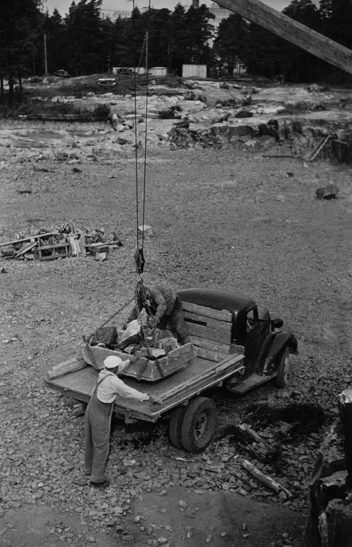 Vaijerikaivinkone ei soveltunut kunnolla tarkkaan pinnan muotoiluun. Siitä syystä viimeistelytyöit tehtiin vielä pitkään jassikalla, johon lopiomiehet siirsivät maata tai kiviä ja kone nosti ja tyhjensi täytetyn jassikan sitten auton lavalle. Kuva Heinonen Eino 1950-1959, Helsingin kaupunginmuseo.