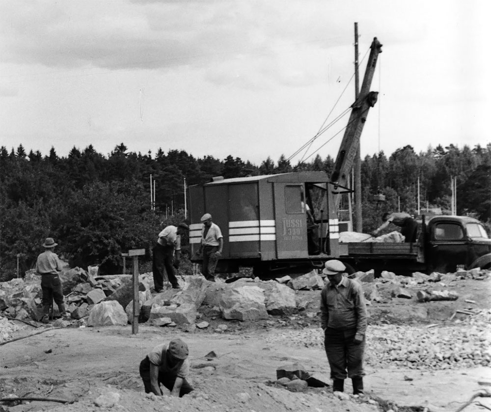 Runkolinjauuditukseen liittyvän bussien liittymäaseman rakentaminen Ruskeasuolle 1955, kaivinkone on Jussi 350. Kaivupuomiin on tehty jatke laittamalla kahdesta U-palkista tehty jatkos varsinaisen kuokkakauha/pistokauhapuomin sisään. Vastaava puomi oli käytössä Koneyhtymä Anderssonilla ja kuvassa oleva kone saattaa olla Anderssonin ensimmäinen Jussi-kaivinkone. Kuva: Okkola Bertel, Helsingin kaupunginmuseo.